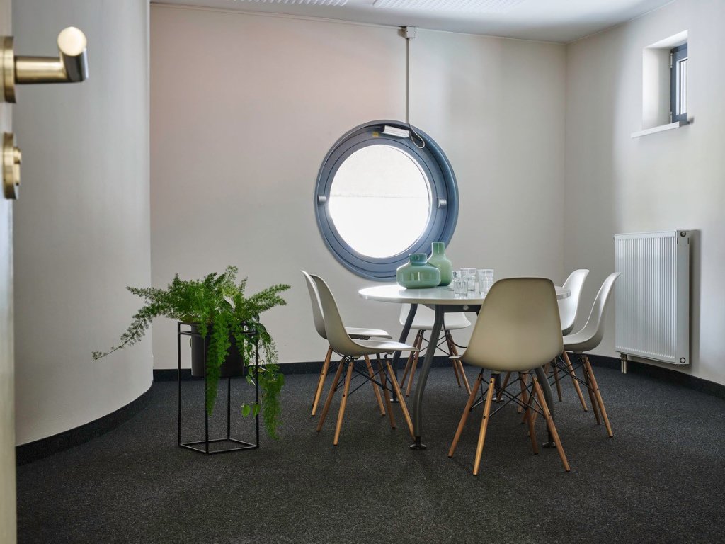 kleiner-runder-weisser-tisch-mit-vier-stuehlen-vor-bullaugen-fenster-gruenpflanzen