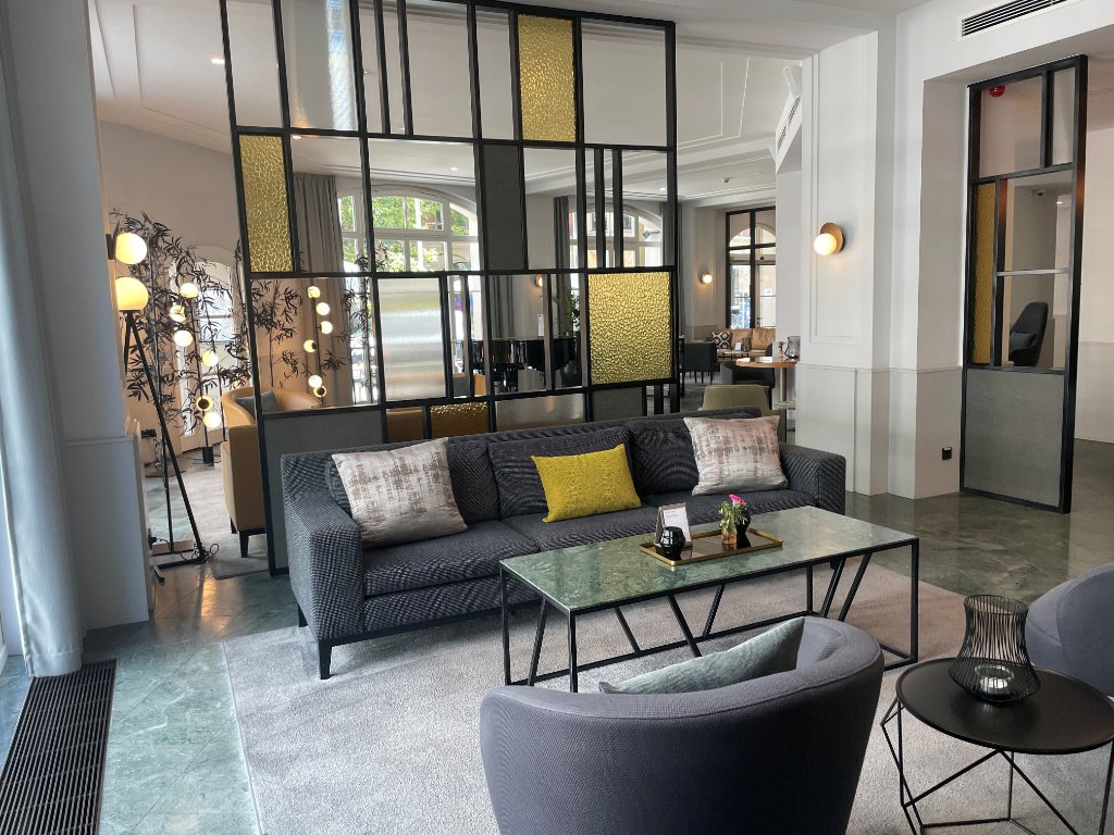 stilvolle lange graue Couch vor Raumtrenner aus Metall und Glas im UNA Berlin-Mitte